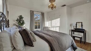 Un dormitorio con cama, escritorio, silla, candelabro y ventana con cortinas.