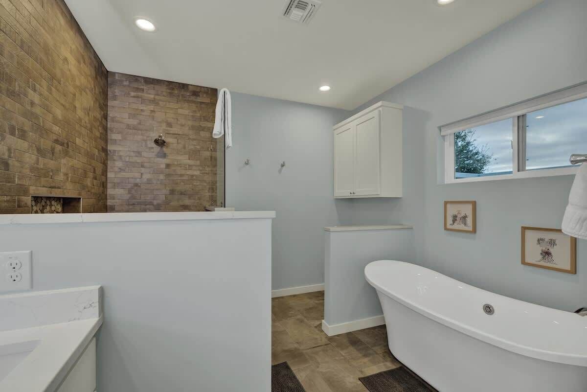A modern bathroom with a freestanding bathtub, a wooden accent wall, and a window providing natural light.