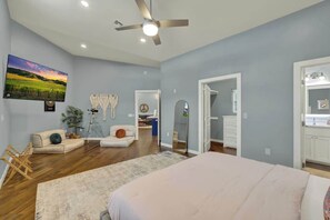 A spacious bedroom with a large bed, a ceiling fan, a TV mounted on the wall, and a view of the adjacent bathroom. - Esperanza Ranch W/hot-tub, Fire Pit, Gorgeous View (Fredericksburg)