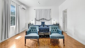 A bedroom with a bed, two armchairs, a ceiling fan, and a window with curtains. - Hill Country Relaxstation Getaway (Fredericksburg)