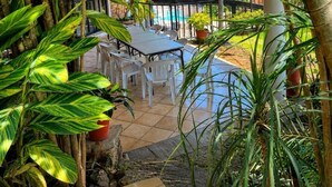 An outdoor patio with a table and chairs, surrounded by plants and a view of a pool.
