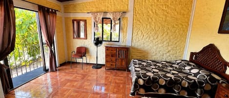 A bedroom with a bed, a desk, a chair, and a fan.