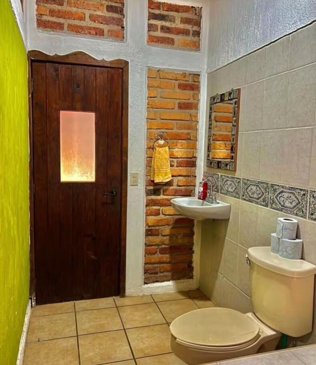 A bathroom with a wooden door, a brick wall, a sink, and a toilet.