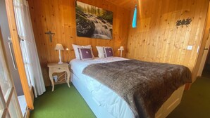 A wooden room with a bed, two nightstands, a painting, and a cross on the wall. - The apartment is in a small 3-storey residence and is ideally located in a quiet area just above the (Gryon)
