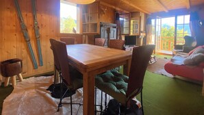 A wooden interior with a dining table, chairs, a fireplace, and a large window. - The apartment is in a small 3-storey residence and is ideally located in a quiet area just above the (Gryon)