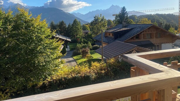 A wooden cabin with a sloped roof, surrounded by lush greenery and a mountain backdrop. - The apartment is in a small 3-storey residence and is ideally located in a quiet area just above the (Gryon)