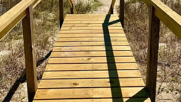 Une promenade en bois menant à une plage, avec des vagues en arrière-plan.