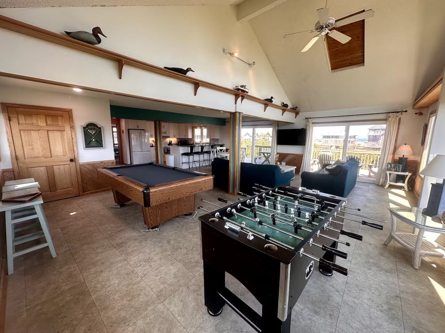A spacious living area with a pool table, foosball table, and a balcony with a view.