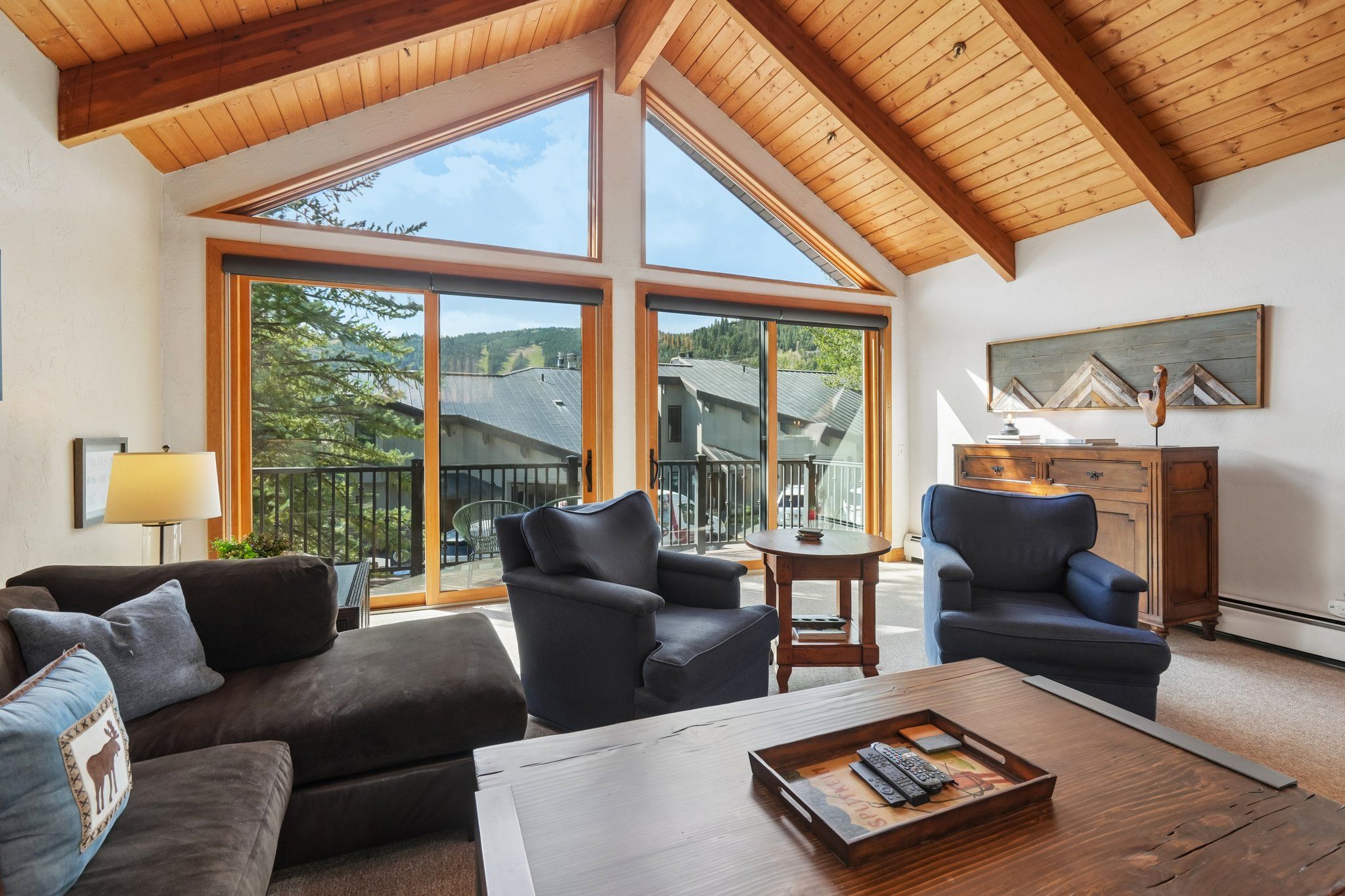 A spacious living room with a high ceiling, large windows, and a view of the surrounding landscape.
