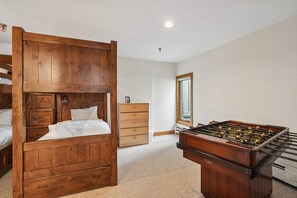 Une chambre avec un lit superposé, une commode en bois, un miroir et une table de baby-foot.