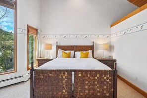 A bedroom with a brick-patterned headboard, two bedside tables with lamps, a large window with a view of trees, and a wall with a sports-themed border.