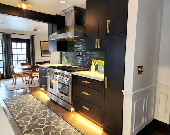 A modern kitchen with dark cabinetry, stainless steel appliances, and a patterned rug. - The Quad Haven & Loft (Casper)