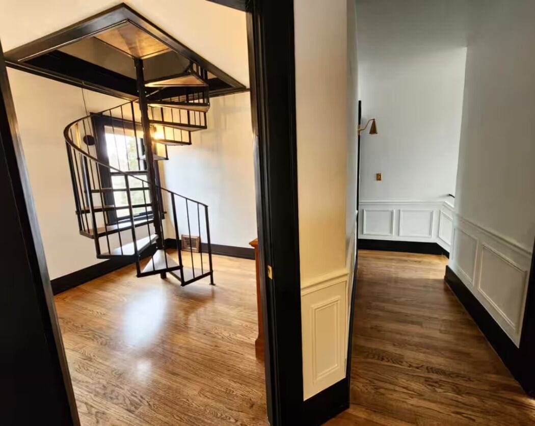 Una escalera de caracol con barandilla negra en una habitación con piso de madera y paredes blancas.
