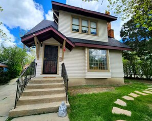 A two-story house with a front porch, a black door, and a small statue on the steps. - The Quad Haven & Loft (Casper)