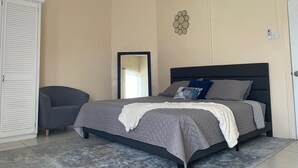 A bedroom with a bed, a chair, a wardrobe, and a decorative wall piece. - Hibiscus Apartment Lovely 2-bedroom apartment with AC in Gros Islet/Corinth (Gros Islet)