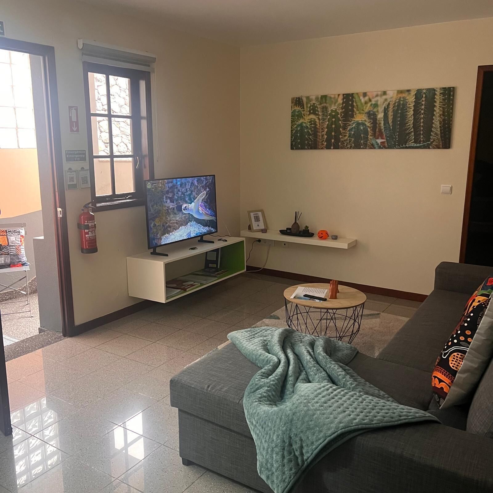 A living room with a grey sofa, a television on a stand, a small round coffee table, and a painting on the wall.