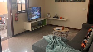 A living room with a grey sofa, a television on a stand, a small round coffee table, and a painting on the wall. - Charming retreat in Machico - 5 min Beach and B Center (Machico)