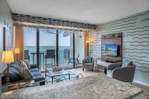 Un salón moderno con un televisor grande, zona de estar y balcón con vista al mar.