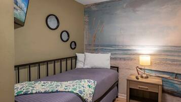A bedroom with a bed, a nightstand with a lamp, and a wall mural of a beach scene.