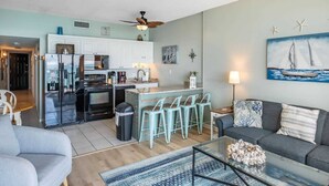 A modern kitchen with a refrigerator, microwave, and stove, a dining area with bar stools, a living room with a sofa, and a painting of a sailboat. - Royal Garden Resort 1514 (Murrells Inlet)
