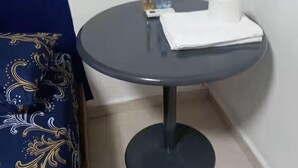A small round table with a dark surface, a bottle of water, a roll of toilet paper, and a small container of tissues. - En la 96 (Cancún)