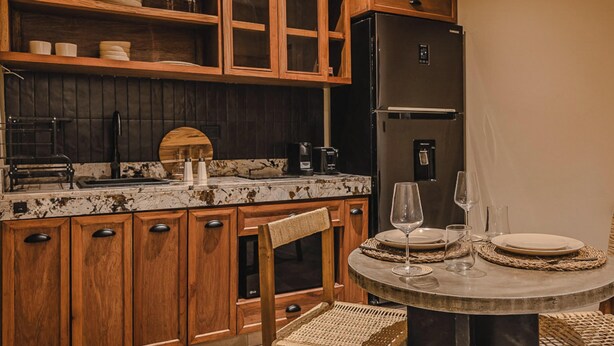 A kitchen with wooden cabinets, a black refrigerator, and a dining area with a round table and chairs. - JUNAB HOUSE - APARTMENT 4 (El Cuyo)