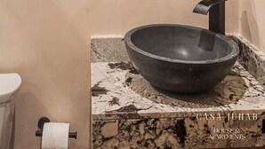 A bathroom with a round mirror, a black vessel sink, and a towel dispenser. - JUNAB HOUSE - APARTMENT 4 (El Cuyo)