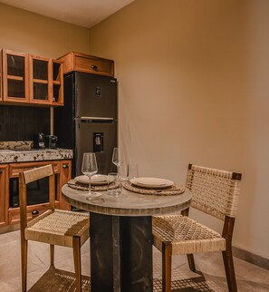 A dining area with a round table, two chairs, a black refrigerator, wooden cabinets, and a coffee maker.