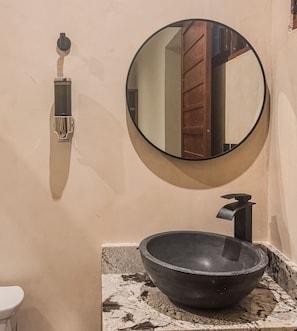 A bathroom with a round mirror, a black vessel sink, and a towel dispenser.