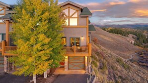 A two-story house with a balcony, a garage, and a view of a hilly landscape. - Spruce Ride Villa 714-H I Great Views I Bunk Room I Gas Fire Table I Discounted Attractions (Fraser)