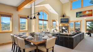 A spacious living area with a large wooden dining table, comfortable seating, and large windows offering mountain views. - Spruce Ride Villa 714-H I Great Views I Bunk Room I Gas Fire Table I Discounted Attractions (Fraser)