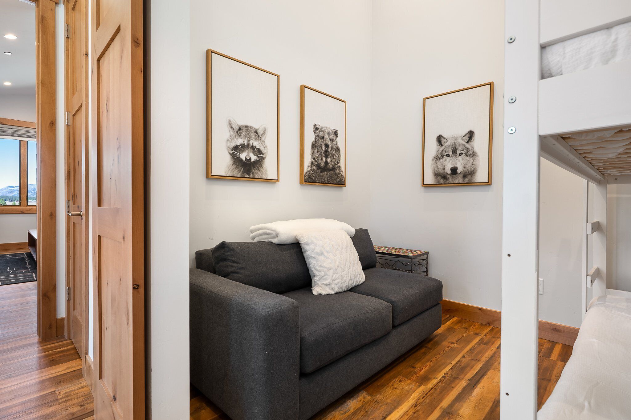 Una sala de estar moderna con un sofá gris, una manta blanca y láminas enmarcadas de animales en la pared.