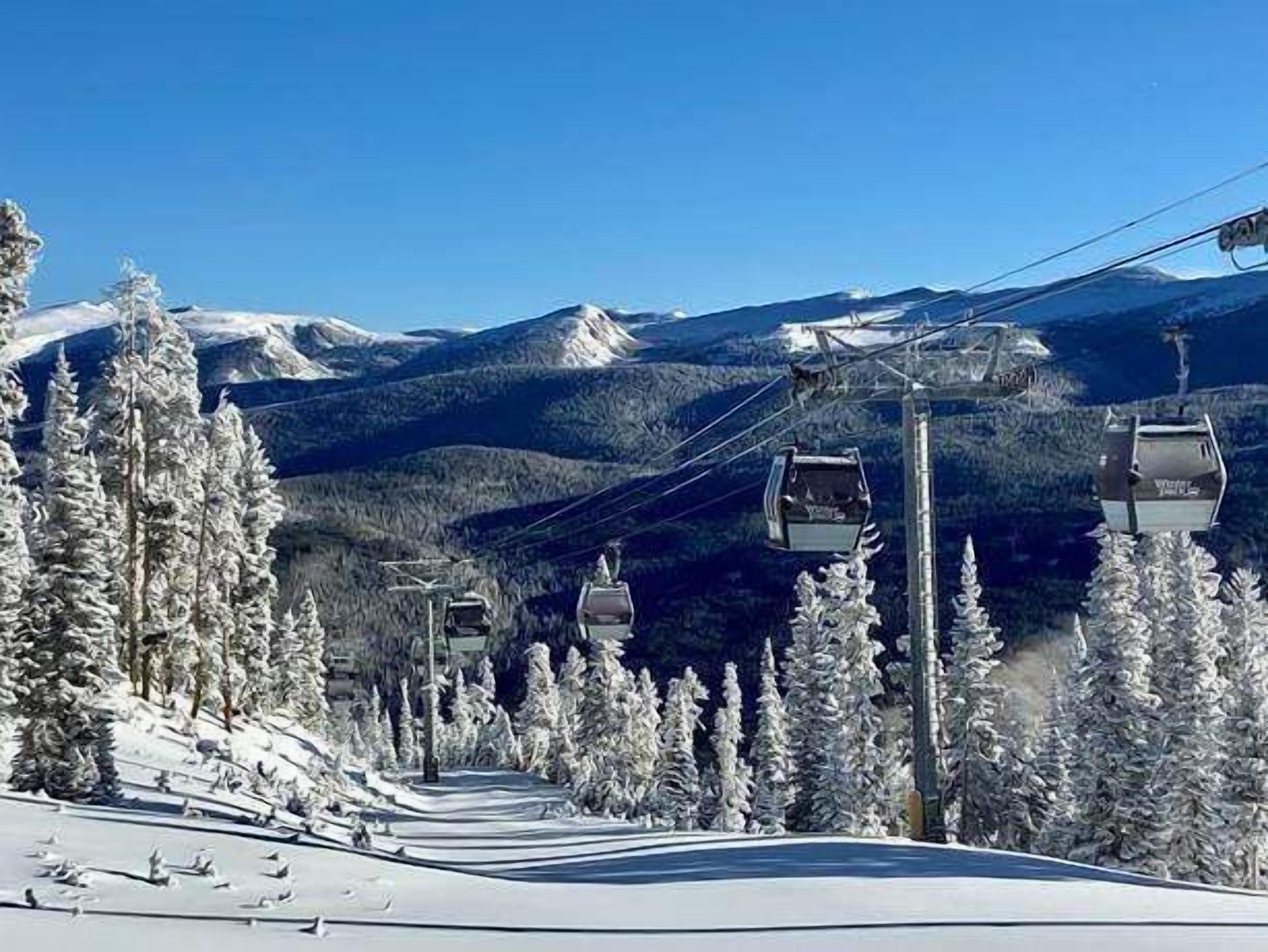 A ski lift with cabins, snow-covered trees, and mountains in the background.
