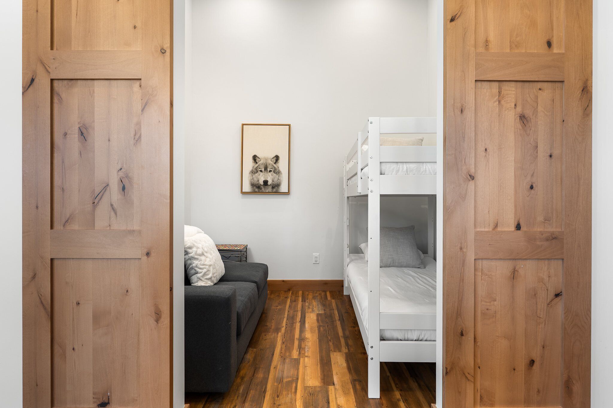 Une pièce avec un lit superposé, un canapé, un tableau encadré au mur et un plancher en bois.
