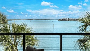 Une vue sur une étendue d’eau, avec un pont au loin, des palmiers et un bâtiment doté d’un balcon.