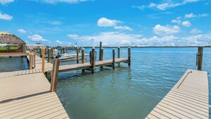 Une jetée en bois s’étendant sur une étendue d’eau calme, avec une structure surmontée d’un toit de chaume et un ciel dégagé.