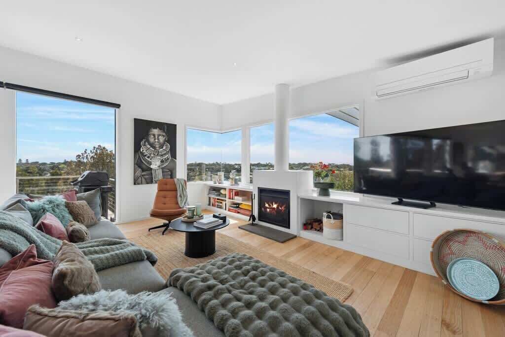 A modern living room with a fireplace, a large flat-screen TV, and a sofa with fluffy cushions.