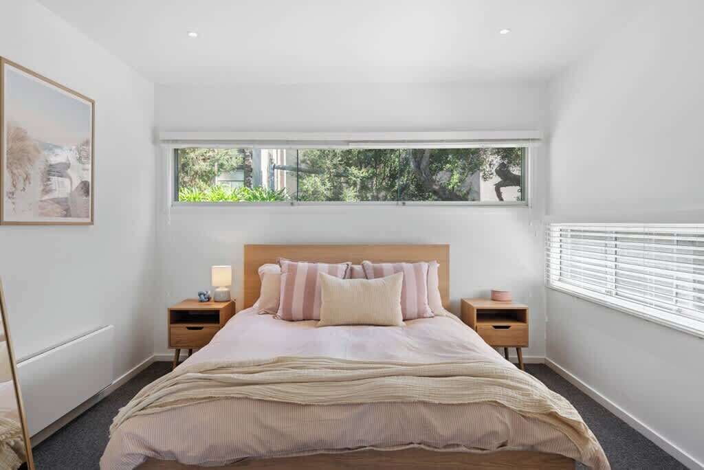 A bedroom with a large window, a bed with striped bedding, two bedside tables, and a nightstand.