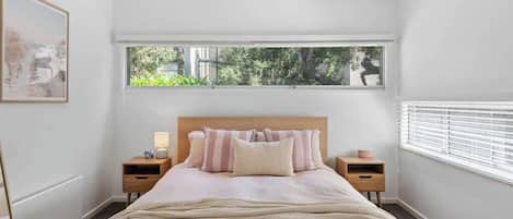 Ein Schlafzimmer mit großem Fenster, einem Bett mit gestreifter Bettwäsche, zwei Nachttischen und einem Beistelltisch.