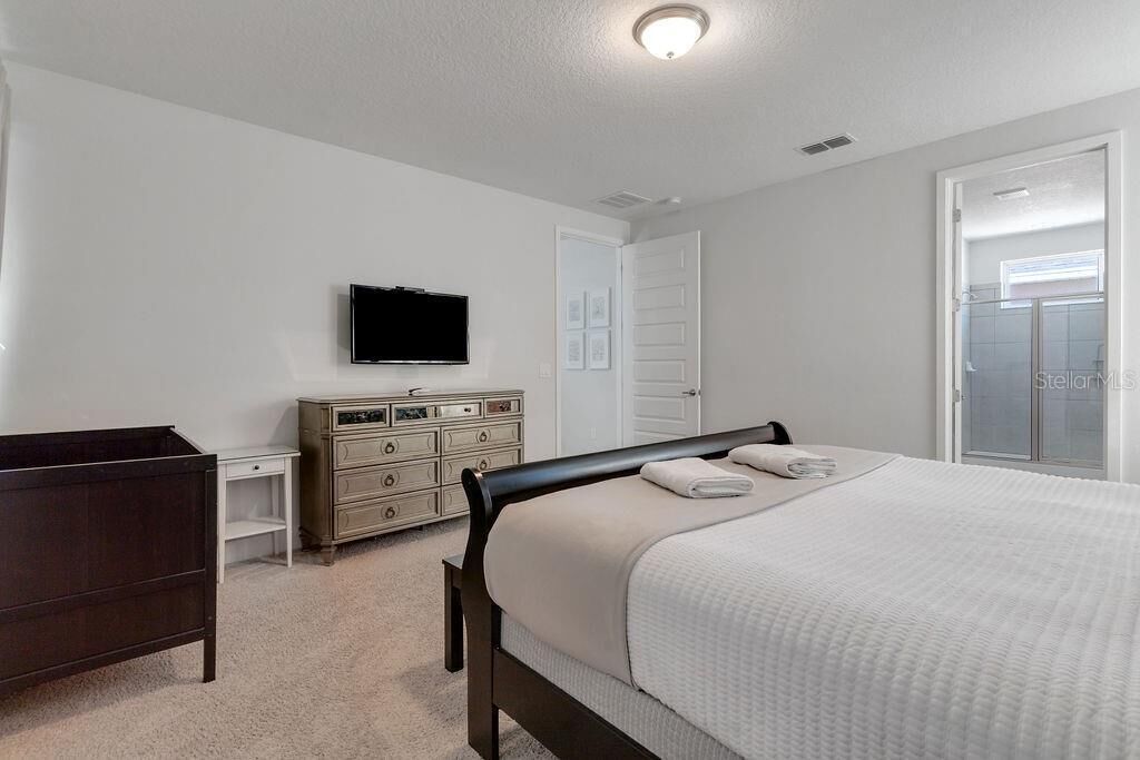 Une chambre à coucher comprenant un lit, une commode, un téléviseur et une porte donnant accès à une salle de bain.
