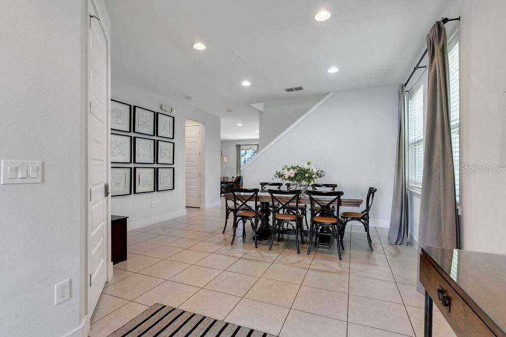 A spacious dining area with a high ceiling, recessed lighting, and a staircase leading to an upper level.