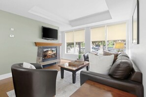 A living room with a fireplace, a sofa, a television, and a window with a view of the outside.