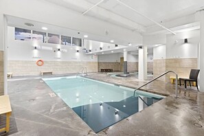 A swimming pool with a glass barrier, benches, and a lifebuoy on the wall.