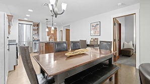 Un comedor moderno con una mesa de madera, sillas con cojines negros, un banco y una araña.