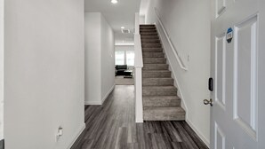 A modern interior with a carpeted staircase, white walls, and a hardwood floor. - Beautiful New Build + Central Location + King Bed & Tv's in Every Room (Montgomery)