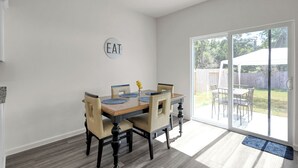 A dining area with a table set for four, a sliding glass door to a backyard, and a 'EAT' sign on the wall. - Beautiful New Build + Central Location + King Bed & Tv's in Every Room (Montgomery)