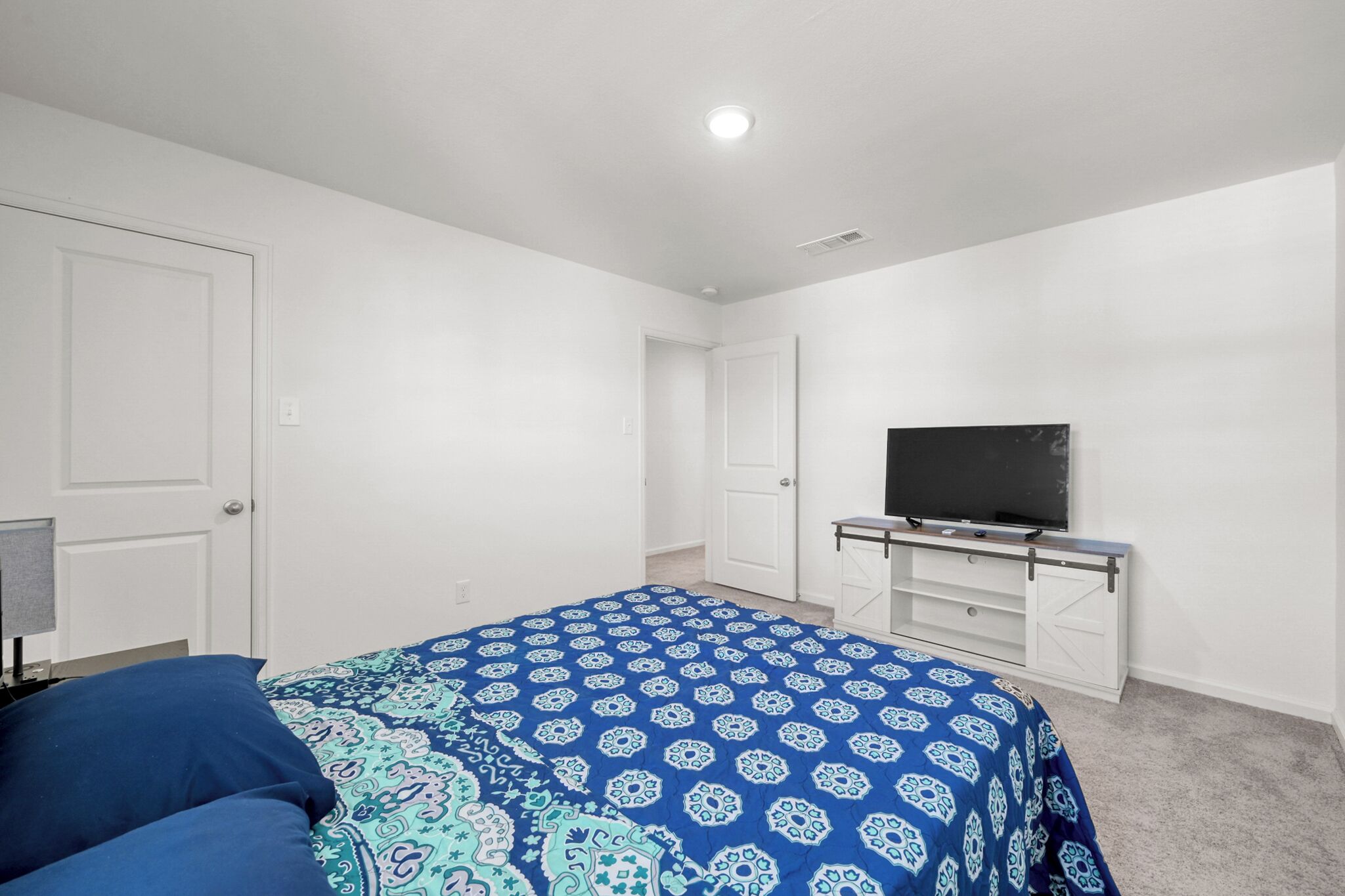 A bedroom with a bed, a TV on a stand, and white walls.