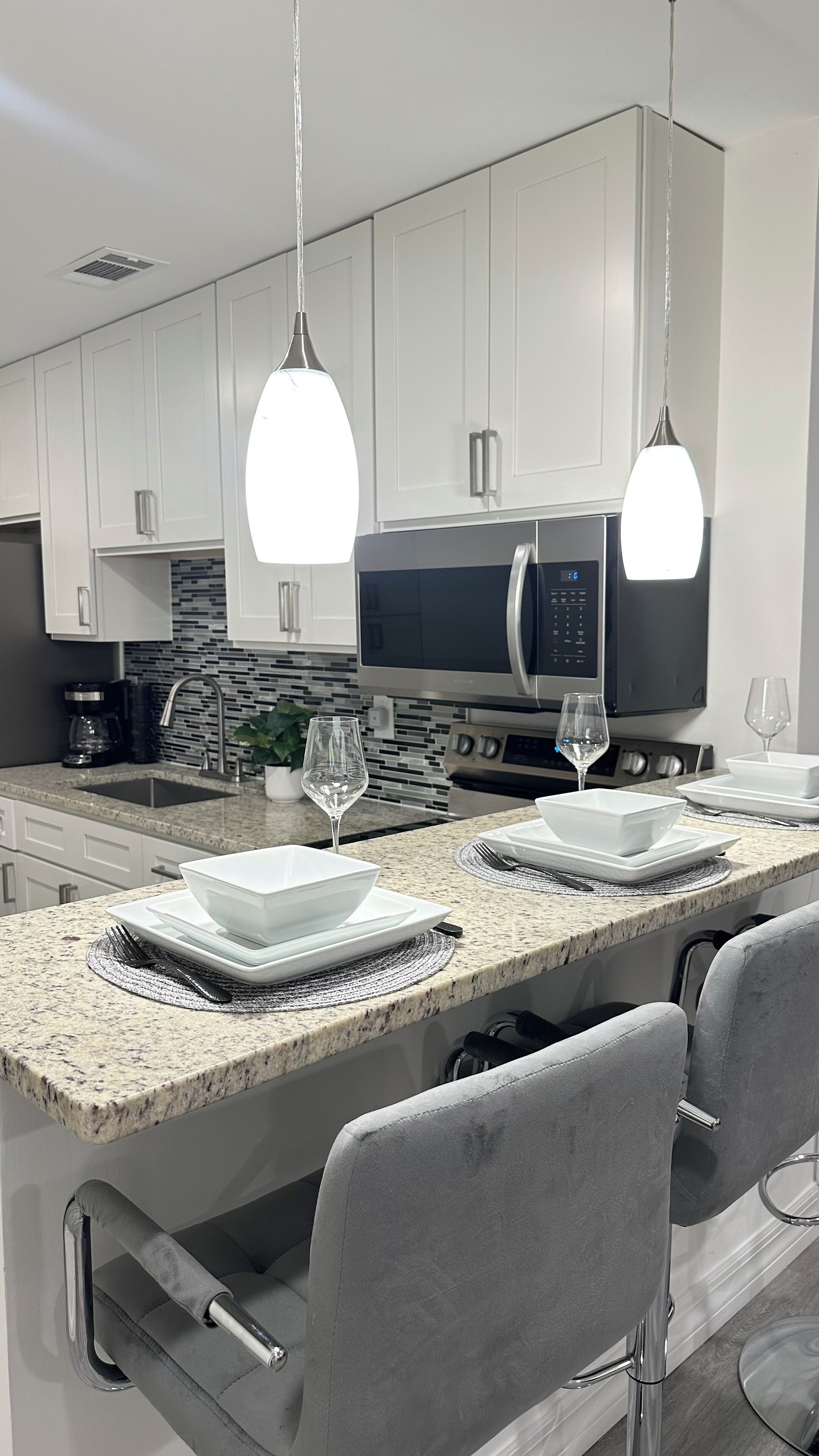 A modern kitchen with white cabinets, a granite countertop, a microwave, and two pendant lights.