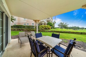 A patio area with a table and chairs, a covered seating area, and a view of a well-maintained lawn and buildings in the background. - Centre Court Rio, Near Disney, Perfect for Golf, Water Park (Kissimmee)