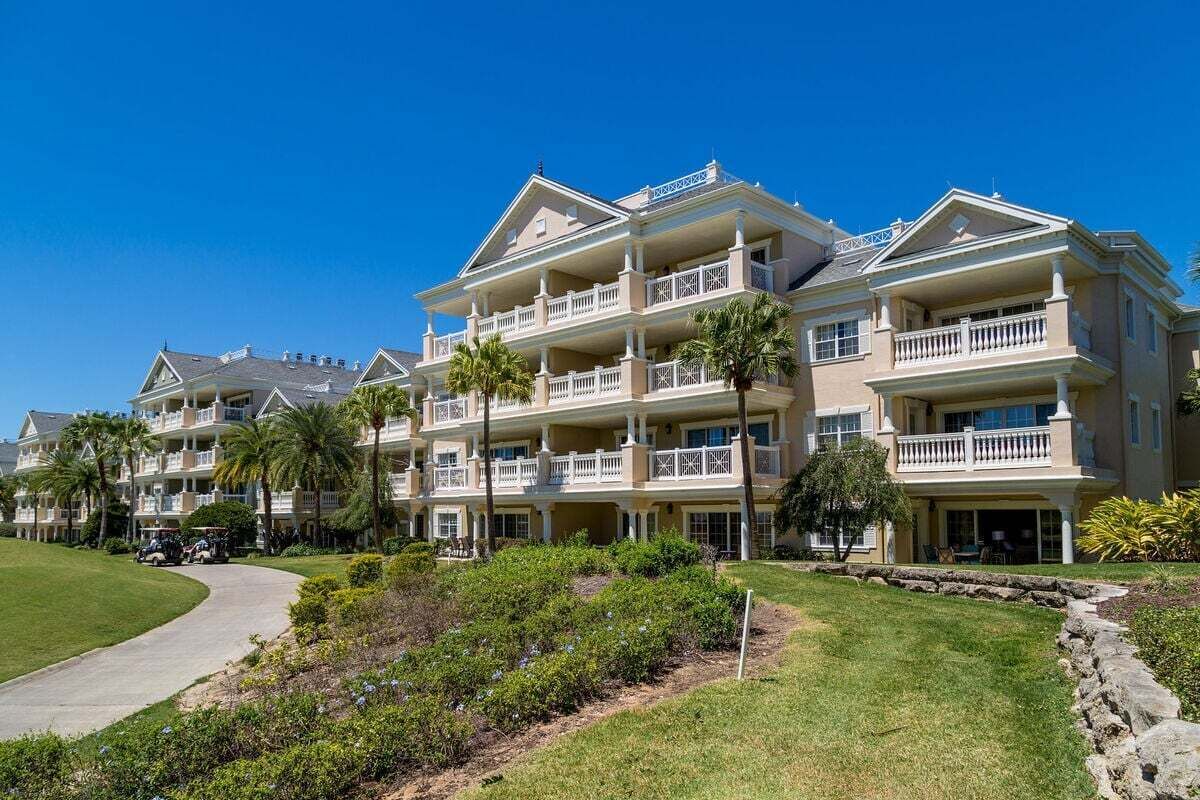 A multi-story hotel with balconies, a well-maintained lawn, and a clear sky.